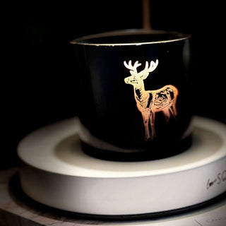 Black candle with deer design on a white candle warming lamp against a dark background