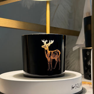 Close-up of a black cylindrical candle with a deer design on a reflective surface.