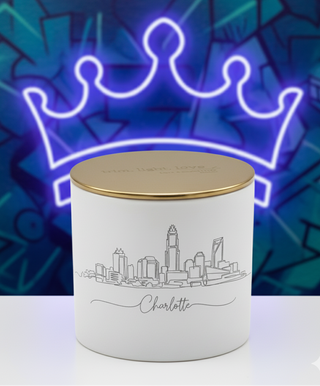 White container with gold lid featuring a cityscape design against a blue graffiti wall with a neon crown.