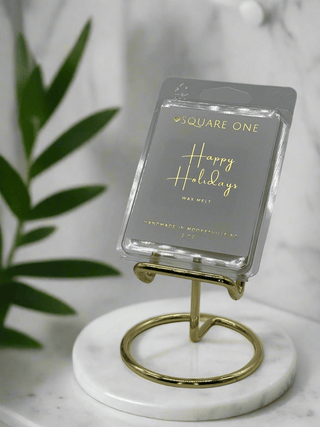 Happy Holidays Wax Melt on white marble and gold stand with green plant on side  - Love Square One