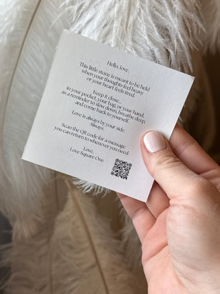 Hand holding a small piece of paper with text and a QR code on a feather background