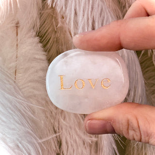Hand holding a white soap with 'LOVE' engraved on it against a fluffy beige background