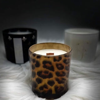 Candle in a leopard print glass container on a textured surface with other candles in the background.