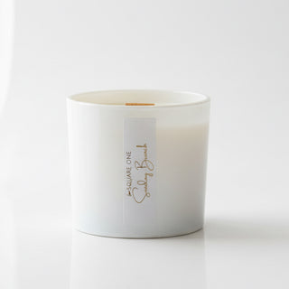 White candle in a cylindrical container with a label on a wooden surface