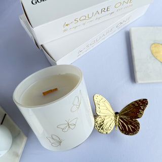 White candle with gold butterfly decorative element on a light purple background