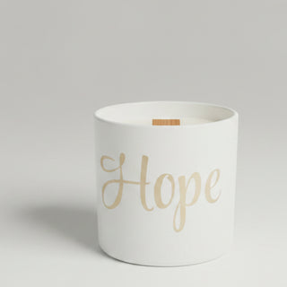 A collection of candles in white containers and boxes, including one with a leopard print pattern and one featuring the word 'Hope' in gold script.
