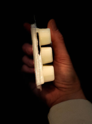 Hand holding a small container with three white cubes against a dark background