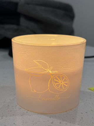 Lit candle with lemon design on a light peach jar