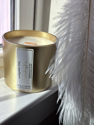 Gold candle holder with a label on a white surface with feathers