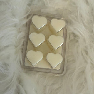 Heart-shaped wax melts in a clear container on a fluffy white surface