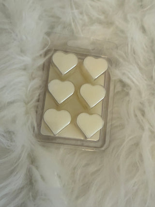 Heart-shaped wax melts in a clear container on a fluffy white surface