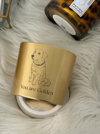 Gold candle jar with dog illustration and 'You are Golden' text on a fluffy white surface.