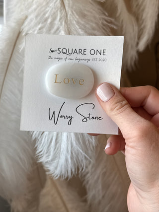 Hand holding a card with a stone and 'Worry Stone' text on a fluffy white surface