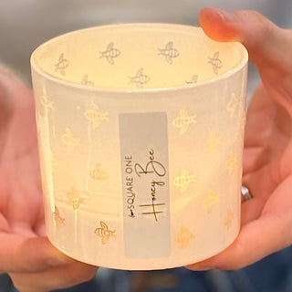 Candle with 'Square One Honey Bee' label held by a hand