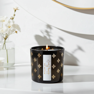 Candle in a black container with decorative honey bee patterns on a white surface.