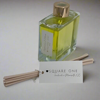 Happy Holidays Reed Diffuser: A luxury fragrance set with a square glass bottle labeled Papyrus & Citrus, metallic cap, and rattan reeds, designed to evoke cozy winter nights with a fresh Christmas tree aroma.