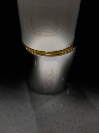 White candle container with gold rim on a dark surface