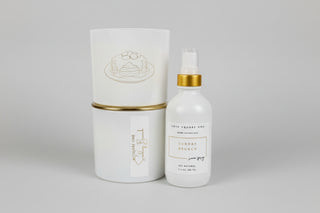 White candle stacked with another white candle with gold lid and white bottle of room spray with gold cap on a countertop. ai enhanced image