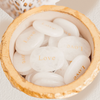 White stones with 'Love' engraving in a wooden bowl on a light background