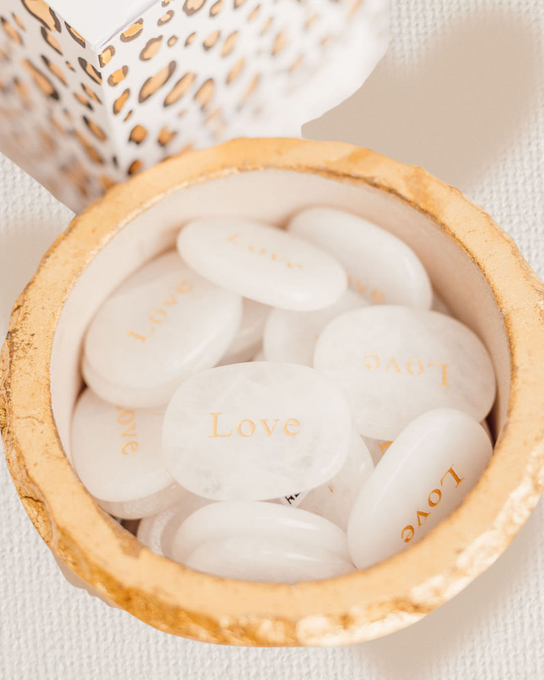 White stones with 'Love' engraving in a wooden bowl on a light background