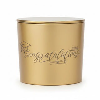 A gold metal candle tin next to its white packaging box. The tin features the word 'Congratulations' printed in black script, and the box has a white label reading 'Square One Candlewax & Leather'.