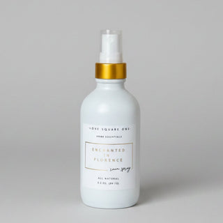 A white room spray bottle of Enchanted in Florence, featuring a gold collar and clear spray nozzle, resting on a white backdrop that was ai generated.