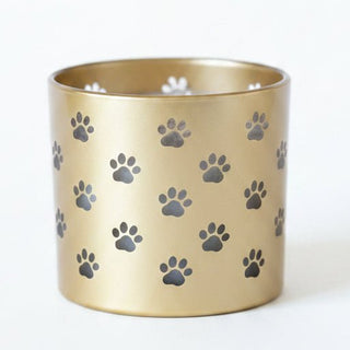 A cylindrical gold metal candle holder or tumbler with a repeating pattern of dark gray paw prints, shown on a plain white background.