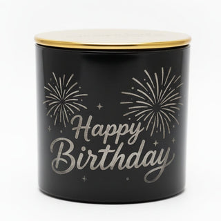 A black candle tin with a gold lid, featuring 'Happy Birthday' in etched script and fireworks.