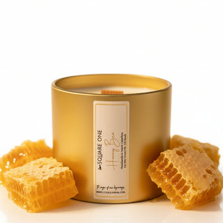 A large gold candle jar filled with wax, featuring a white label that reads 'SQUARE ONE Honey Bee'.