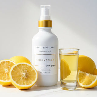 A white room spray bottle of Love Square One Limoncello home essentials, featuring a gold collar and clear spray nozzle, resting on a marble surface with ai added lemons.