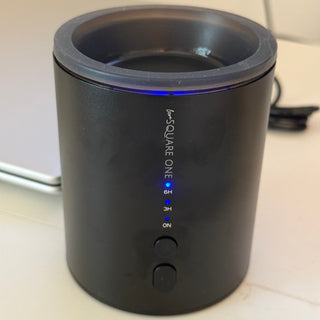 A black cylindrical wax warmer device labeled 'love SQUARE ONE' with blue LED indicator lights, sitting on a light-colored surface.