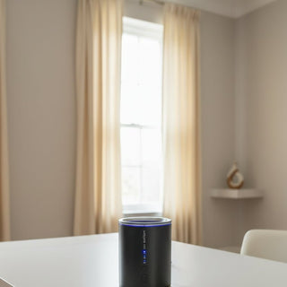 A black cylindrical projector mounted on a white wall, with a power cable visible at the top and blue indicator lights turned on.