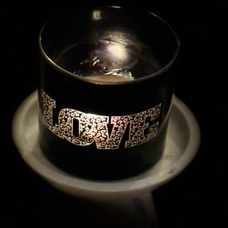 A black glass candle holder with the word 'LOVE' sitting on a white candle holder against a dark background.