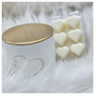image of white candle with gold lid and heart shaped wax melts in background