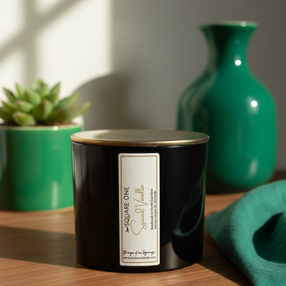 Close up of a black Square One Spice and Vanilla candle tin with a white and gold label, stacked on a white cylindrical base.