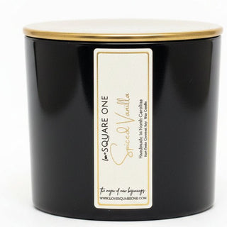 A black square jar candle with a gold-toned lid and a cream label reading 'Square One Spiced Vanilla' by Love square one