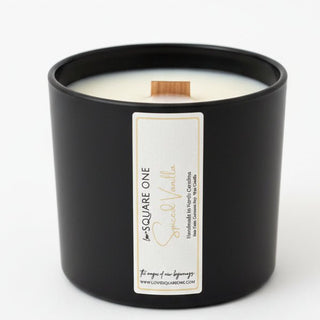 Black Love Square One Special Vanilla candle with white wax and a cinnamon stick wick on a white shelf.⠋