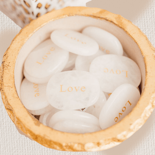 White stones with 'Love' engraving in a wooden bowl on a light background