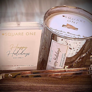 Square One Happy Holidays Wax Melt and candle set, showcasing a wax melt clamshell and a candle in a metallic jar, accompanied by a gold-tone wick trimmer, embodying cozy holiday fragrances.